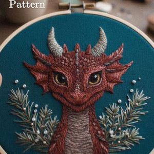 May include: Embroidered dragon hoop art with a teal background. The dragon is red with detailed stitching, featuring horns, scales, and large eyes. The design includes sprigs of greenery and the text "Pdf Pattern" and "lumellu.com".