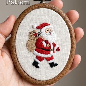 May include: An oval embroidery hoop with a wood-grain frame containing a white fabric panel featuring a hand-stitched Santa Claus carrying a tan sack. The text PDF Pattern is in the top left corner and Lumellu is at the bottom.
