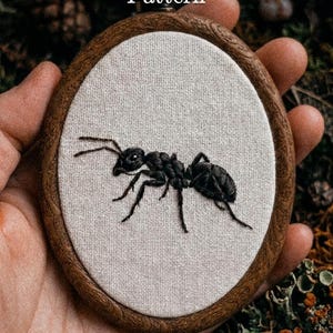 Könnte beinhalten: Ein ovaler Stickrahmen mit einem detaillierten schwarzen Ameisenmuster auf hellem beigefarbenem Stoff. Der Holzrahmen hat eine dunkelbraune Oberfläche. Der Text "Pdf Pattern" steht oben und die Website "lumellu.com" unten.