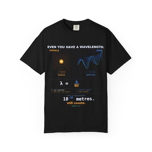 Könnte beinhalten: Ein schwarzes T-Shirt mit einem weißen, orangefarbenen und blauen Grafikdruck. Der Text lautet: EVEN YOU HAVE A WAVELENGTH. PARTICLE, WAVE, lambda equals h over mv, und yours is approximately 10^-35 metres. still counts. QUANTUM & CO.