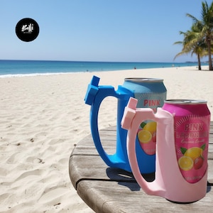 Puede incluir: Dos portlatas de plástico con asas integradas, uno en azul claro y otro en rosa claro, que sujetan cada uno una lata de aluminio de limonada rosa. Los soportes presentan un detalle en forma de estrella en la parte superior del asa.
