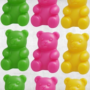 Könnte beinhalten: Ein Raster aus bunten Gummibärchen in Grün, Pink und Gelb. Die Bären sind in Reihen und Spalten angeordnet, jeder mit einem lächelnden Gesicht und der klassischen Gummibärenform. Der Hintergrund ist eine helle, strukturierte Oberfläche.