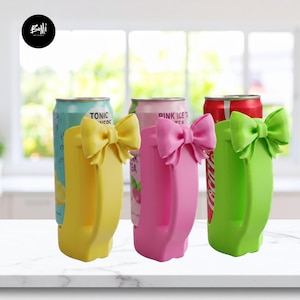 Può includere: Tre portabevande colorati con dettagli a fiocco. I supporti sono gialli, rosa e verdi, ciascuno con un fiocco abbinato. All'interno dei supporti sono visibili lattine di bibite. I supporti hanno un manico.