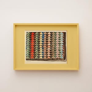 Op de afbeelding: Een ingelijste print met een quiltpatroon bestaande uit herhalende driehoekige vormen in diverse kleuren, waaronder rood, groen, blauw, geel en roze. Het kunstwerk zit in een gele lijst met een bijpassende gele passe-partout.