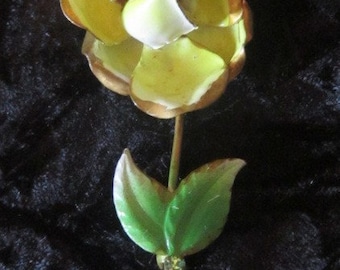 May include: A yellow and brown enamel rose brooch with green leaves and a rhinestone accent. The brooch is on a black velvet background.