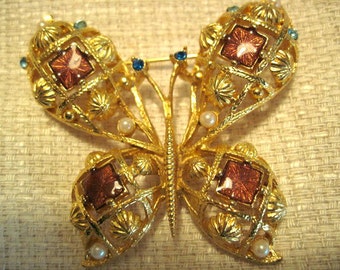 Puede incluir: Un broche de mariposa de oro con detalles intrincados. Las alas están hechas de una delicada malla de alambre con acentos de esmalte rojo y blanco. La mariposa tiene piedras preciosas azules y blancas.