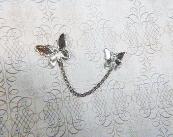 May include: A silver chain with two butterfly charms. The butterflies have clear rhinestones on their wings.