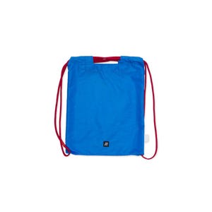 May include: A vibrant blue drawstring bag with red drawstrings and a red handle. The bag features a small, square black logo at the bottom and a white tag on the side. The bag is made of a lightweight material.