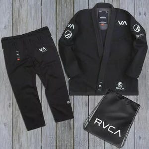 Puede incluir: Un conjunto de uniforme de artes marciales negro, que incluye una chaqueta, pantalones y una bolsa con cordón. Los logotipos "VA" y "RVCA" en blanco adornan la chaqueta y los pantalones. El conjunto se muestra sobre una superficie de madera.