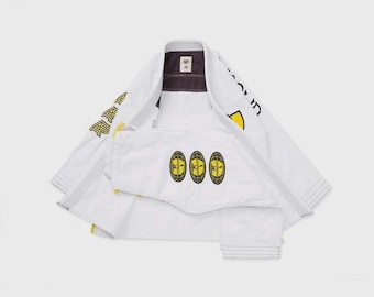 May include: White Jiu-Jitsu uniform with yellow and black accents. The jacket has yellow lettering and patches, and the pants feature three embroidered patches. The uniform is laid out on a light background.