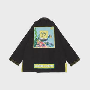 May include: Black martial arts gi with a yellow trim and the text "ALBINO & PRETO". The back of the gi features a colorful graphic of SpongeBob SquarePants in a fighting pose, surrounded by underwater elements.