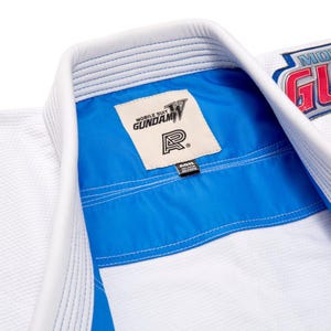 May include: White martial arts uniform with blue detailing and stitching. The collar has a blue lining and a tag with the text "MOBILE SUIT GUNDAM". The uniform is made of a textured fabric.