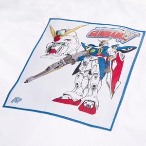 May include: White fabric with a blue border featuring a colourful illustration of a Gundam robot. The robot is primarily white, blue, red, and yellow, with a large gun. The text "MOBILE SUIT GUNDAM W" is also visible.