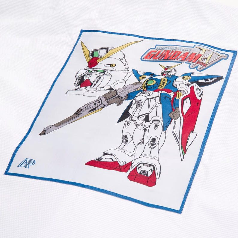 May include: White fabric with a blue border featuring a colourful illustration of a Gundam robot. The robot is primarily white, blue, red, and yellow, with a large gun. The text "MOBILE SUIT GUNDAM W" is also visible.