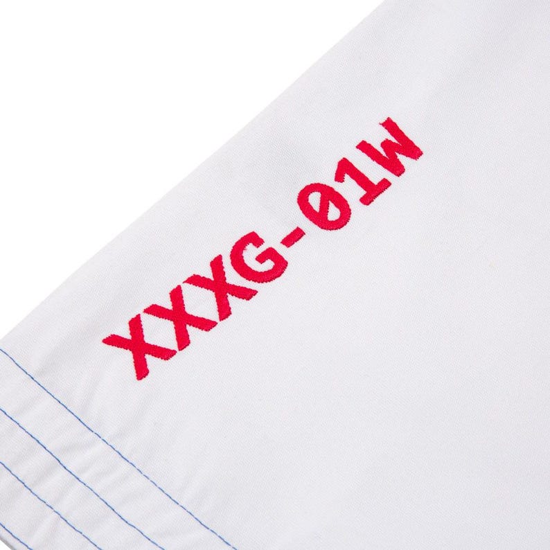 May include: Close-up of white fabric with red embroidered text: "XXXG-01W". Blue stitching is visible along the edge. The image focuses on a section of the fabric.