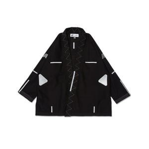 May include: Black kimono-style jacket with white geometric accents. Features white stitching along the edges and a triangular patch on the front. The jacket has a relaxed fit and a minimalist design.