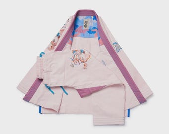 May include: A light pink martial arts uniform set, including a jacket and pants. The jacket has purple trim and a blue and pink patterned interior. The pants have a drawstring waist. The set features embroidered floral and dragon designs.
