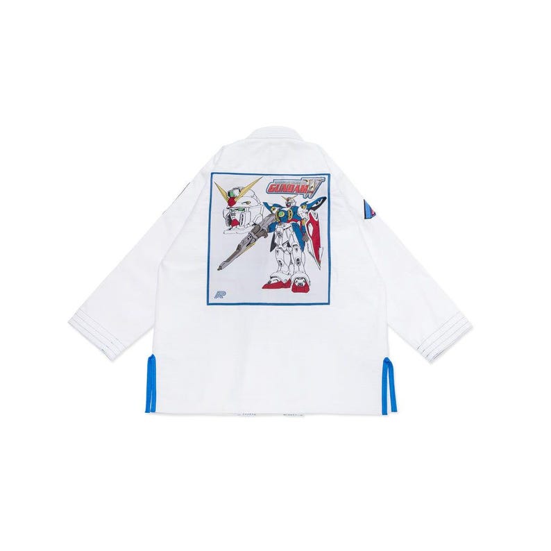 May include: White martial arts gi featuring a colourful robot graphic on the back. The robot is blue, red, and white, with the word "GUNDAM" above it. Blue accents are on the sleeves and sides.