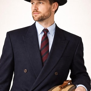May include: A navy blue double-breasted suit with a black fedora hat and a striped tie. The suit has a classic design with a light blue dress shirt underneath. A vintage suitcase is held in the arm.