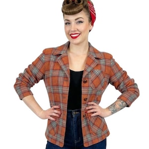May include: An orange and grey plaid blazer with a notched collar, button closure, and a chest pocket. The jacket is worn over a black top and paired with dark blue jeans. The model is wearing a red bandana.