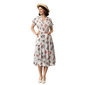 May include: A vintage-style floral print dress with a V-neckline and short sleeves. The dress features a wrap-style bodice and a midi-length skirt. The floral pattern includes red, purple, and green flowers on a white background. A straw hat with a black band completes the look.