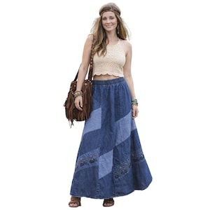 May include: A woman in a cream crochet halter top and a long denim skirt with patchwork and embroidery. She carries a brown fringed shoulder bag and wears a headband and bracelets, embodying a bohemian aesthetic.