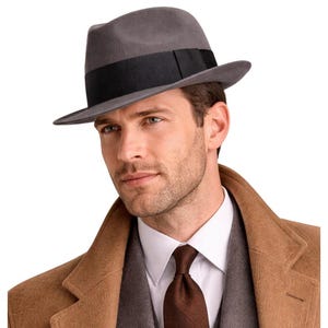 Op de afbeelding: Een grijze fedora hoed met een zwarte band. De hoed wordt gedragen met een bruine overjas, een grijs pak, een wit overhemd met kraag en een bruine stropdas. De hoed heeft een klassiek, tijdloos ontwerp.