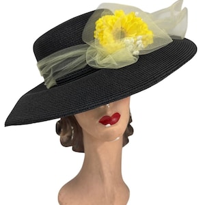 Puede incluir: Un sombrero de paja negro de ala ancha con una flor amarilla y un lazo de tul amarillo.
