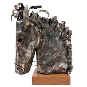 May include: A metal sculpture of a horse's head, crafted from welded metal pieces. The sculpture features a dark, textured finish with details like a mane and bridle. It is mounted on a rectangular wooden base, showcasing an industrial art style.