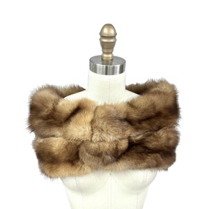 Puede incluir: Una estola de piel marrón con una textura suave y esponjosa. La estola se muestra en un maniquí blanco.