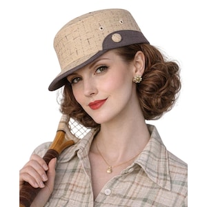 May include: A tan and brown hat with a structured brim and a decorative button. The hat has a textured weave pattern and is accented with a darker brown band. The hat is worn with a plaid shirt and a tennis racket.
