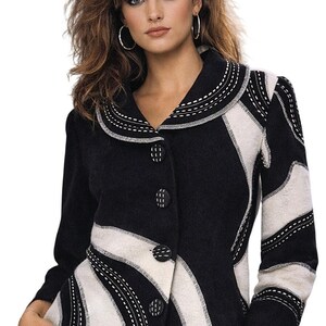 May include: Black and white patterned jacket with a unique design. The jacket features a collar and button closure. The white sections are outlined with white stitching. The model is wearing silver hoop earrings and a silver bracelet.