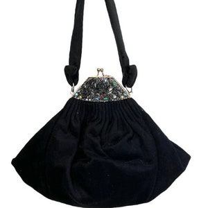 Puede incluir: Un bolso de noche de terciopelo negro con un cierre decorativo con un diseño floral y pedrería de colores.