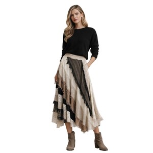 May include: A black long-sleeve sweater paired with a tiered midi skirt. The skirt features panels of beige, brown, and black fabrics with lace and fringe details. The outfit is completed with ankle boots.