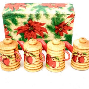 Puede incluir: Conjunto de cuatro teteras de madera con asas rojas y un diseño navideño. Las teteras están en una caja con un patrón de poinsettia roja.