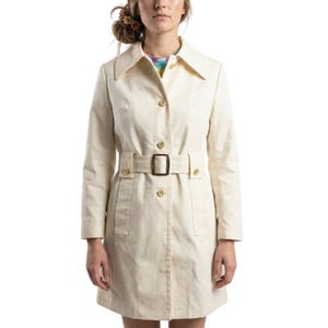 May include: Cream-colored trench coat with a belted waist and large collar. The coat features gold-colored buttons and a matching belt buckle. The coat has two front pockets and is made of a smooth fabric.
