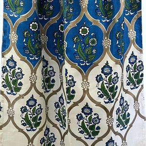 May include: Curtain panel with a blue and white floral pattern. The design features blue and green flowers on a white background, set within a gold-coloured trellis. The top edge is pleated, and the fabric is patterned.