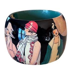 Può includere: Una ciotola rotonda decorativa con esterno nero con un disegno dipinto di donne in abiti vintage. L'interno della ciotola è di colore verde scuro. Le donne sono raffigurate in rosa, bianco e verde.