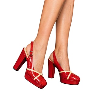 May include: Red patent leather platform slingback heels with a thick block heel and a cream-colored accent. The shoes have a buckle closure and a rounded toe. The heels are approximately 4 inches high.