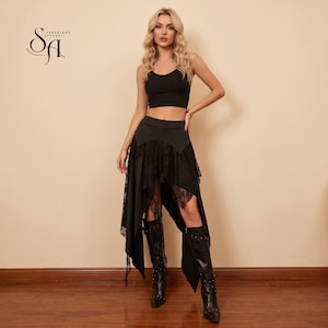 May include: A black sleeveless crop top paired with a high-waisted black skirt featuring an asymmetrical hemline, layered lace panels, and a solid waistband. The outfit is completed with black knee-high boots. The Serenique Apparel logo is visible.