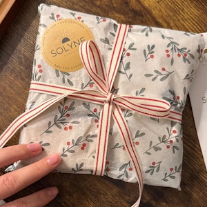 May include: A wrapped package with a floral design and a red and white striped ribbon tied in a bow. The package is sealed with a round sticker that reads "SOLYNE" and "THANK YOU FOR YOUR PURCHASE AND FOR SUPPORT".