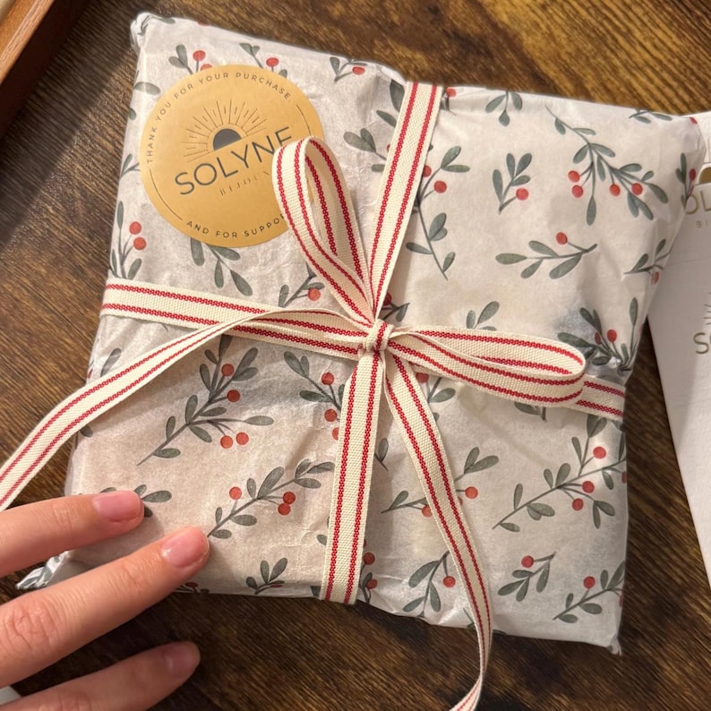 May include: A wrapped package with a floral design and a red and white striped ribbon tied in a bow. The package is sealed with a round sticker that reads "SOLYNE" and "THANK YOU FOR YOUR PURCHASE AND FOR SUPPORT".