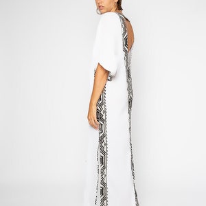 Peut inclure: Une robe longue blanche orn&eacute;e d'un motif g&eacute;om&eacute;trique noir et blanc sur les c&ocirc;t&eacute;s et le dos. La robe a des manches courtes et un dos nu. Le mod&egrave;le est tourn&eacute; dos &agrave; la cam&eacute;ra.