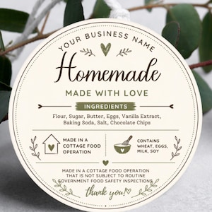 May include: A round, cream-colored tag with dark green text and graphics. It features the words "Homemade," "Made with Love," and "Ingredients," followed by a list of baking items. It includes icons of a house and a bowl, plus safety text.