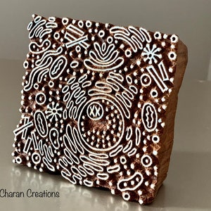 May include: A wooden printing block featuring a white design of abstract shapes, dots, and lines. The design includes the letters "XX" within a circle.