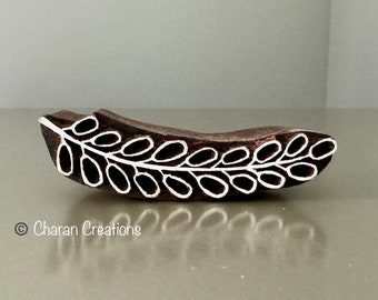 May include: A wooden printing block featuring a white design of a leaf with oval shapes. The block is brown and has a smooth surface.
