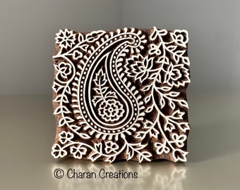 Könnte beinhalten: Ein Holzblock-Stempel mit einem Paisley-Muster und filigranen floralen Details. Der Stempel ist mit einem weißen Design auf einem dunkelbraunen Hintergrund geschnitzt.