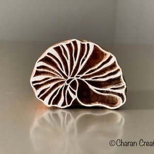 May include: A wooden block printing stamp with a white design of a stylized seashell. The stamp is brown and has a natural wood grain.