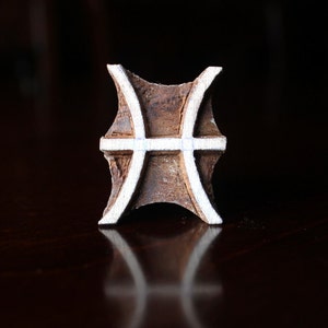 May include: A wooden block stamp with a white outline of the astrological symbol for Pisces.