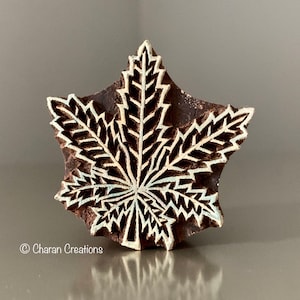 May include: A brown wooden block carved into the shape of a maple leaf. The leaf is detailed with white lines and a white center.